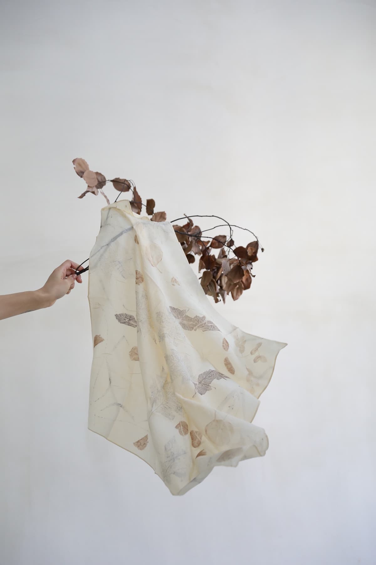 A hand holding a botanical-print textile beside dried branches.