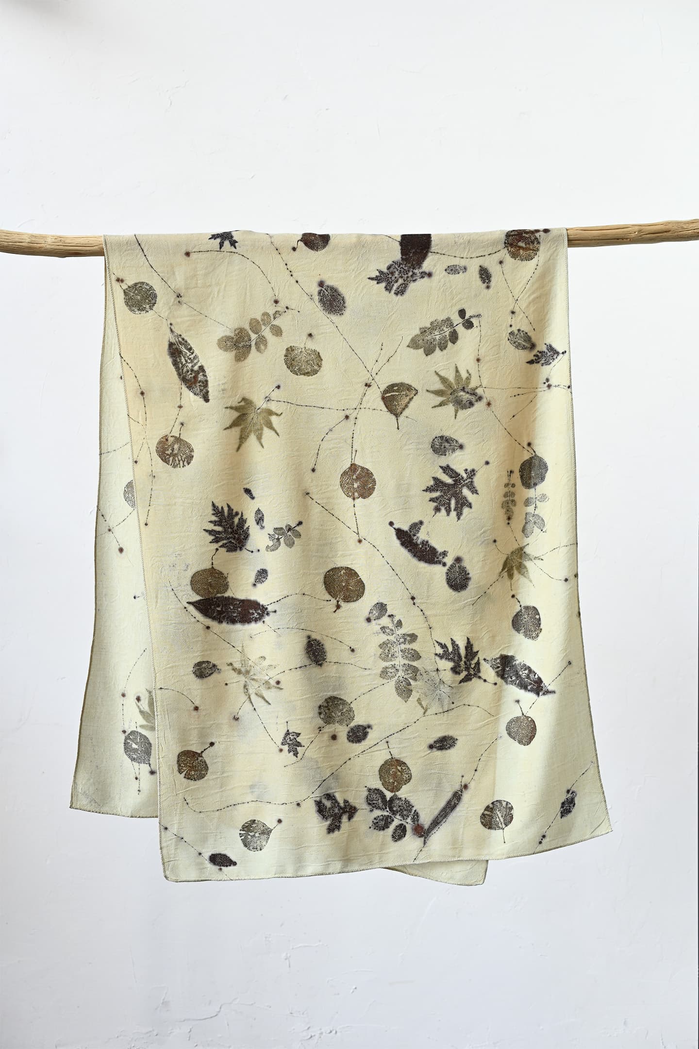 A botanical-print scarf displayed on a branch against a light wall.