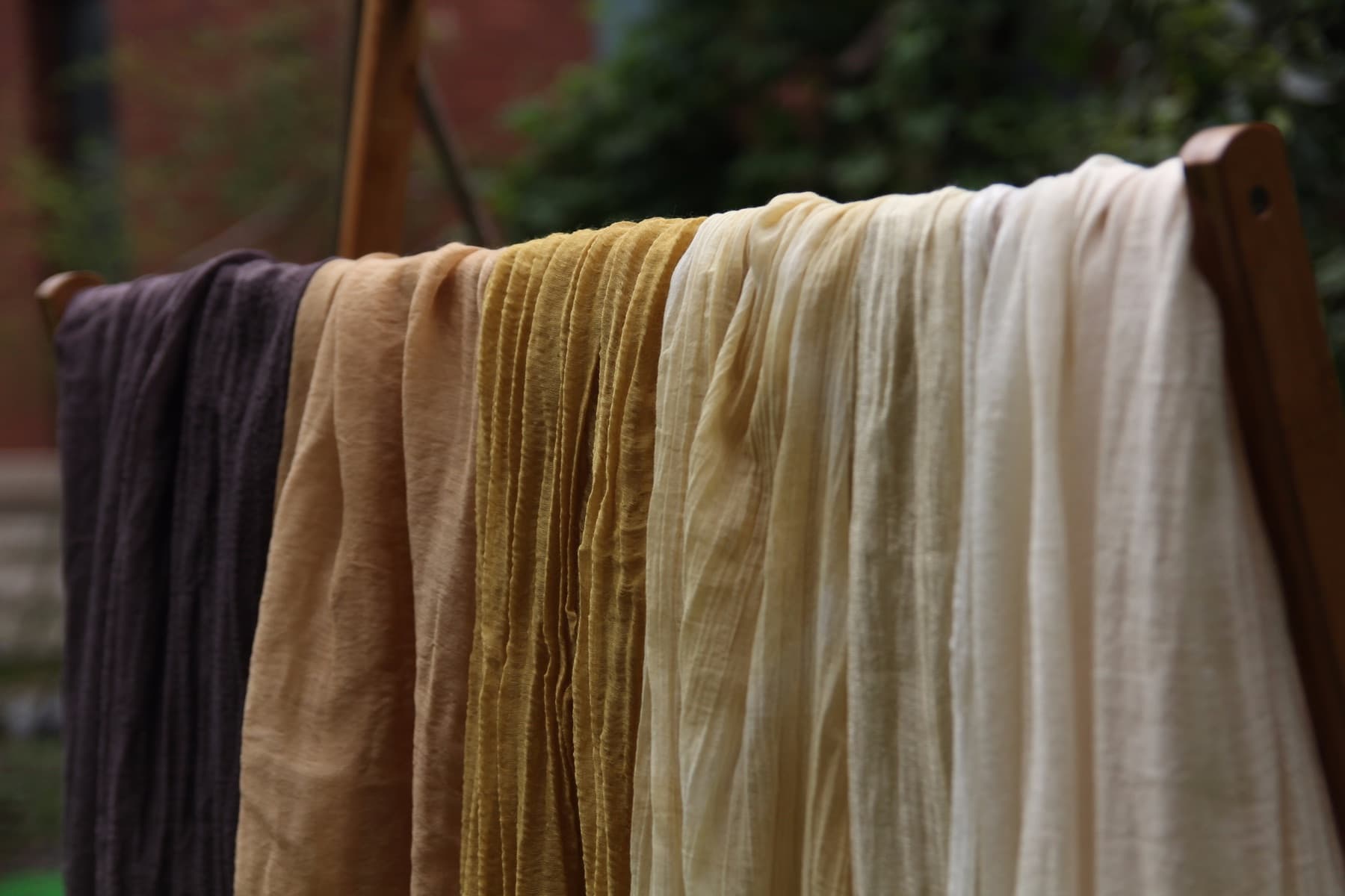 Naturally colored textile samples hanging together on a wooden rail.